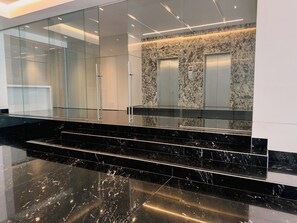 A modern elevator with a marble wall, a glass elevator door, and a black marble staircase. - Roma Residence| Luxury Suite 202 (Mexico City)