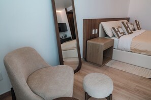 A modern hotel room with a large mirror, a wooden nightstand, a bed with beige bedding, and a round ottoman. - Condesa Residence - Roma Luxury Suite 603 (Mexico City)