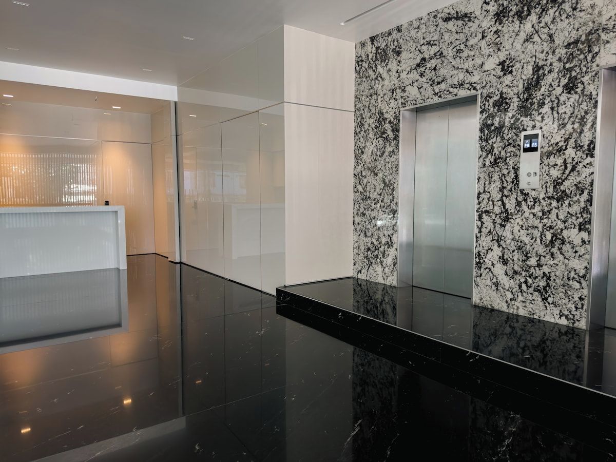 A modern elevator with a granite wall, a glass elevator door, and a control panel.