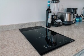 Eine Küche mit einer schwarzen Induktionskochplatte, einer Weinflasche, einem Mixer, einer Kaffeemaschine und einem Wasserkocher.