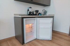 Eine kompakte Küche mit einem integrierten Kühlschrank, einer Kaffeemaschine und einem Wasserkocher auf der Arbeitsfläche.