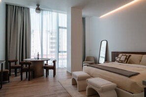 A modern hotel room with a round dining table, a bed with a headboard, a mirror, and a view of the city through large windows. - Condesa Residence - Roma Luxury Suite 303 (Ciudad de México)