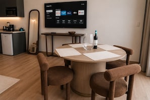 A modern living room with a round wooden table, two brown chairs, a flat-screen TV displaying a smart TV interface, a kitchen area with a microwave, and a coffee maker. - Condesa Residence - Roma Luxury Suite 604 (Mexico City)