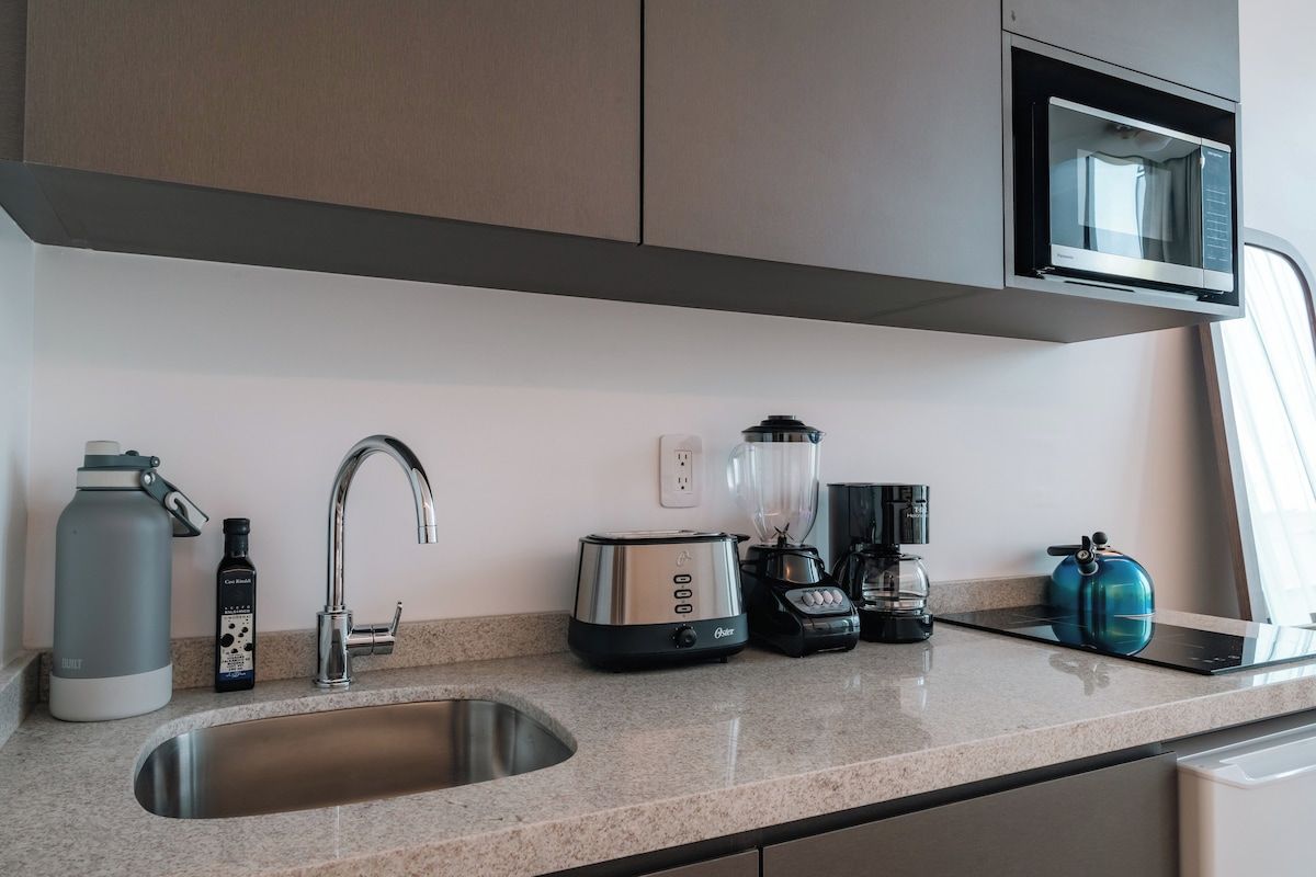 A modern kitchen with a stainless steel sink, a kettle, a toaster, a blender, and a microwave.