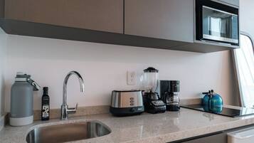 A modern kitchen with a stainless steel sink, a kettle, a toaster, a blender, and a microwave.
