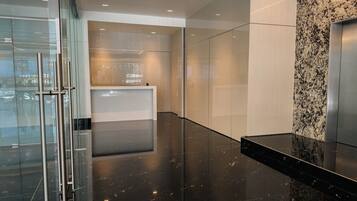 A modern interior with a glass elevator, a reception desk, and a marble wall.