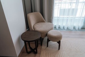 A room with a beige armchair, a round wooden table, and a matching ottoman. - Condesa Residence - Roma Luxury Suite 606 (Mexico City)
