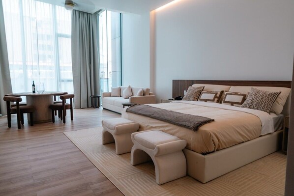 A modern bedroom with a large bed, bedside tables, a seating area with a table and chairs, and a view through large windows. - Condesa Residence - Roma Luxury Suite  304 (Ciudad de México)