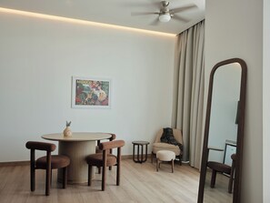 A modern room with a round table, two chairs, a sofa, a small stool, a ceiling fan, a large mirror, and a framed picture on the wall. - Condesa Residence - Roma Luxury Suite 607 (Mexico City)