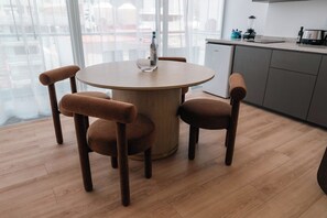 A round wooden table with four brown chairs, a bottle on the table, and a kitchen area with appliances in the background. - Condesa Residence - Roma Luxury Suite  305 (Ciudad de México)