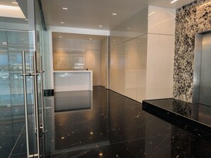 A modern elevator area with reflective black flooring, a glass wall, and a marble wall with a metallic elevator. - Condesa Residence - Roma Luxury Suite  305 (Ciudad de México)