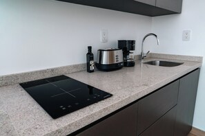 A modern kitchen with a built-in induction cooktop, a coffee maker, a toaster, and a sink. - Condesa Residence - Roma Luxury Suite  305 (Ciudad de México)