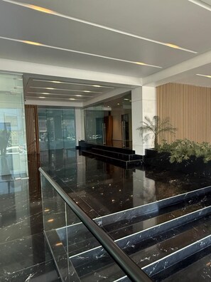 A modern lobby with a marble floor, a staircase, and a reception area with a wooden panel wall. - Condesa Residence - Roma Luxury Suite 401 (Ciudad de México)