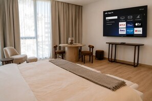Ein Hotelzimmer mit Bett, rundem Tisch mit Stühlen, Wandfernseher und einem Fenster mit Vorhängen.