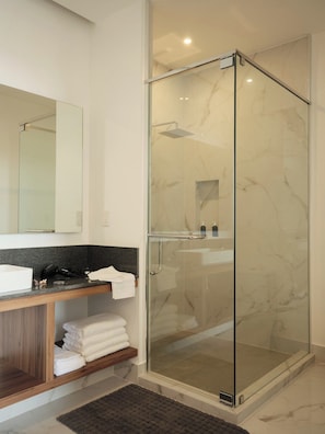 A modern bathroom with a glass-enclosed shower, a marble-tiled wall, a wooden vanity, and a large mirror. - Condesa Residence - Roma Luxury Suite 504 (Mexico City)