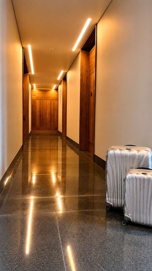 Un couloir d’hôtel avec un sol ciré, des murs lambrissés et une rangée de portes fermées.