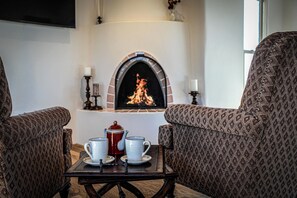 A cozy room with a fireplace, two patterned armchairs, and a table with tea set. - Luxury Above the Pines with Mountain Views (Santa Fe)