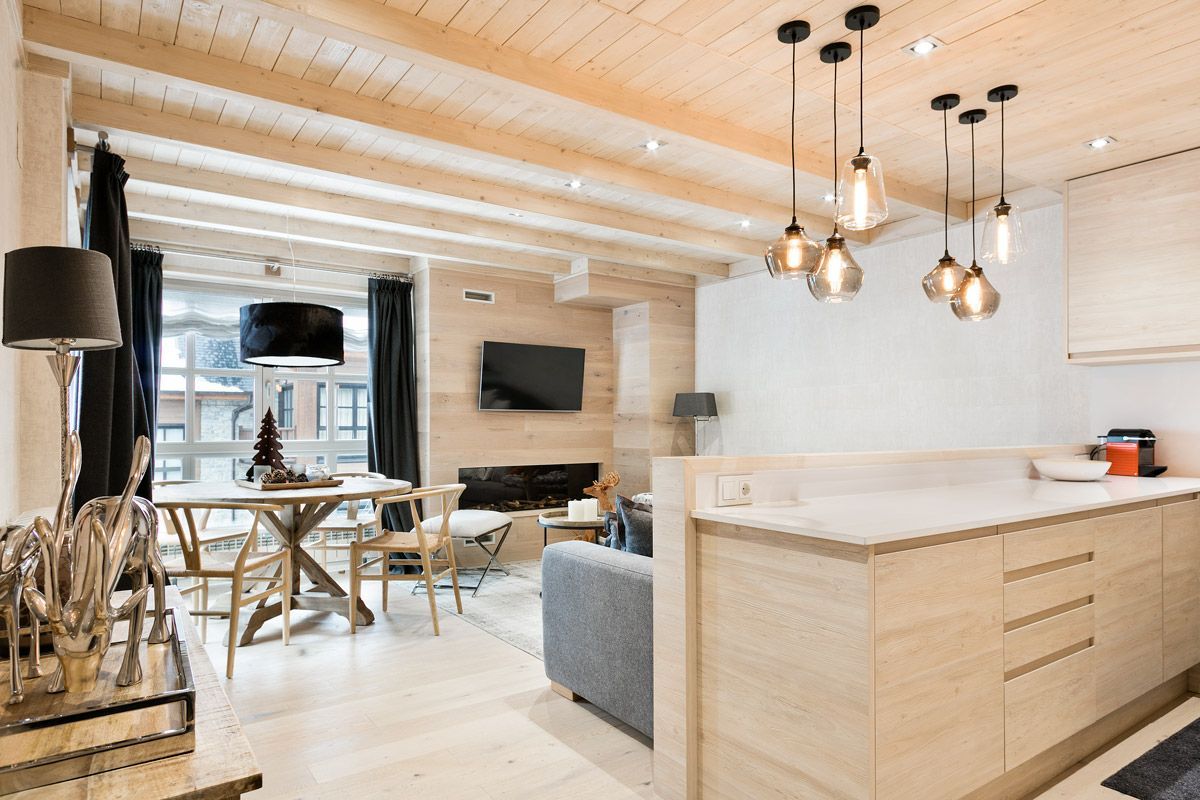 A modern kitchen with wooden cabinets, a dining area with a table and chairs, and a living room with a sofa and a flat-screen TV.
