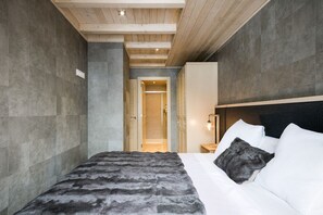 Ein modernes Schlafzimmer mit einem großen Bett, einer Holzbalkendecke und Blick in einen angrenzenden Raum.