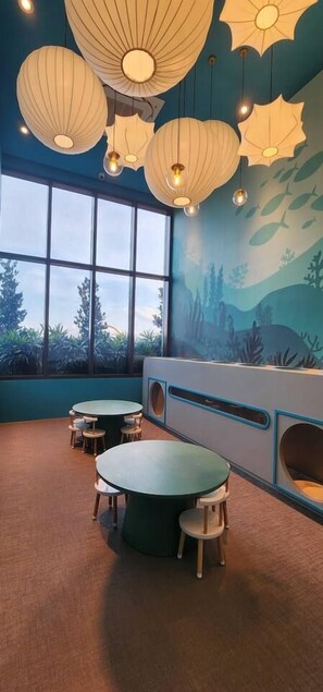 A room with round tables and chairs, a mural of underwater scenery, and hanging lamps.