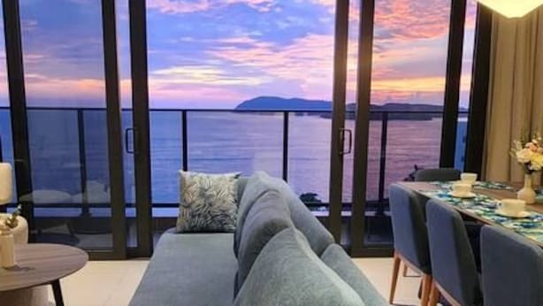 Un balcon avec un canapé et une table à manger, donnant sur une étendue d’eau et offrant une vue sur le coucher de soleil.