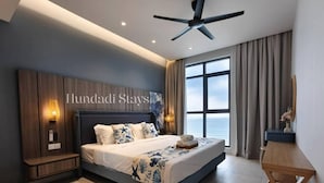 Une chambre d’hôtel moderne avec un grand lit, un ventilateur de plafond, une vue sur la mer et une pancarte indiquant « Hundaldi Stays ».