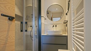 A modern bathroom with a glass-enclosed shower, a round mirror, and a white sink. - Luderna - Dúplex Val de Ruda C42 eth Pletiu (Baqueira)