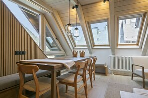 Uma área de refeições com mesa e cadeiras de madeira, um claraboia e vista para o exterior.