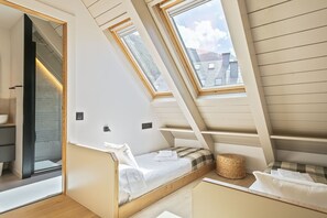 Quarto com teto inclinado, claraboias, uma cama com travesseiro e uma pequena cesta de vime.