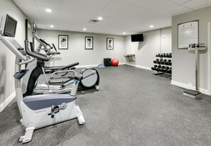A fitness room with treadmills, a stationary bike, a red exercise ball, and a rack of dumbbells.