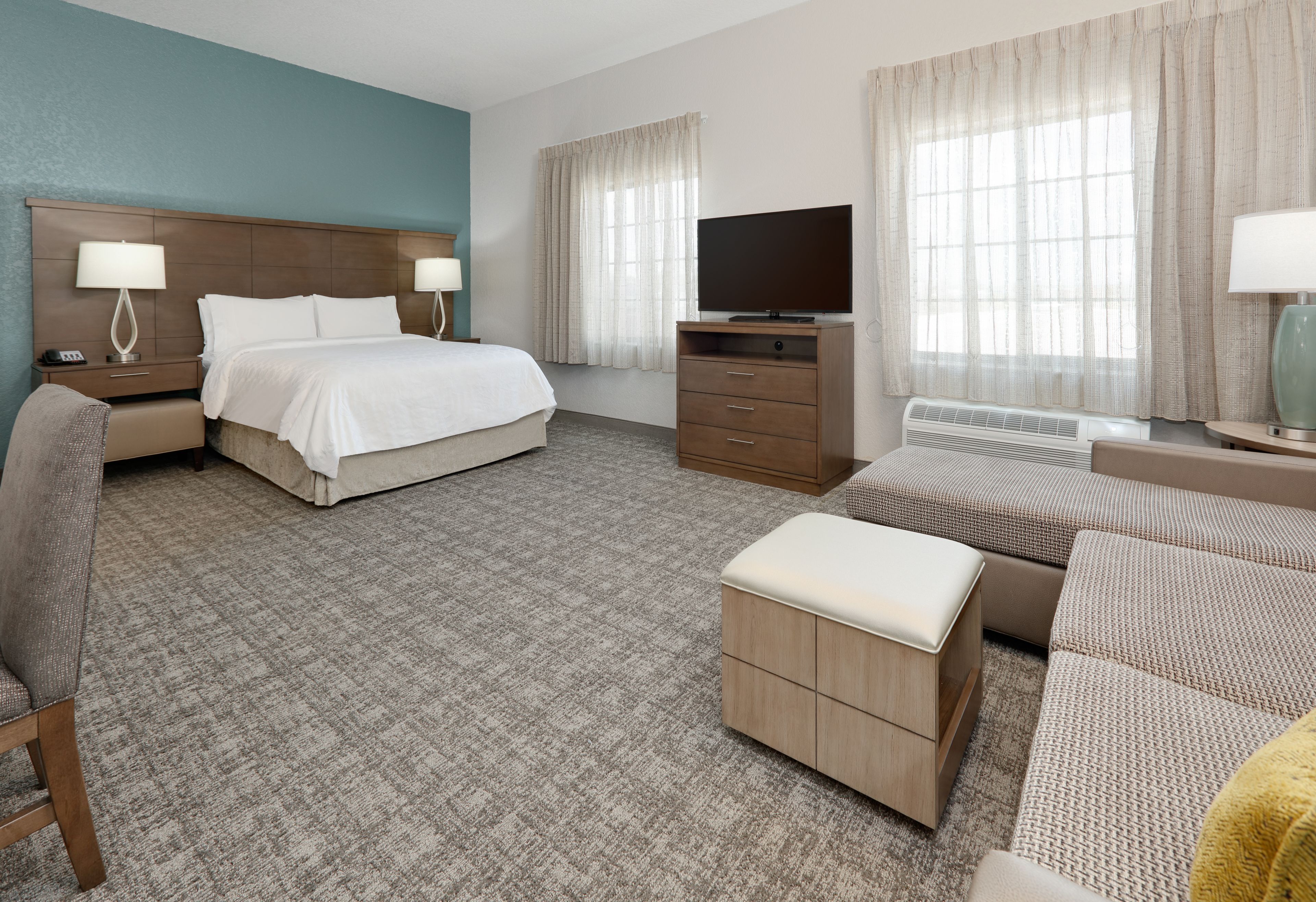 A hotel room with a bed, a TV, a desk, a chair, and a sofa.