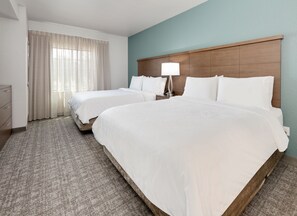 Ein Hotelzimmer mit zwei Betten, einem Nachttisch mit Lampe, einem Schminktisch und einem Fenster mit Vorhängen.
