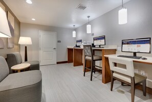 A hotel room with a desk, two chairs, a sofa, a lamp, and two monitors.