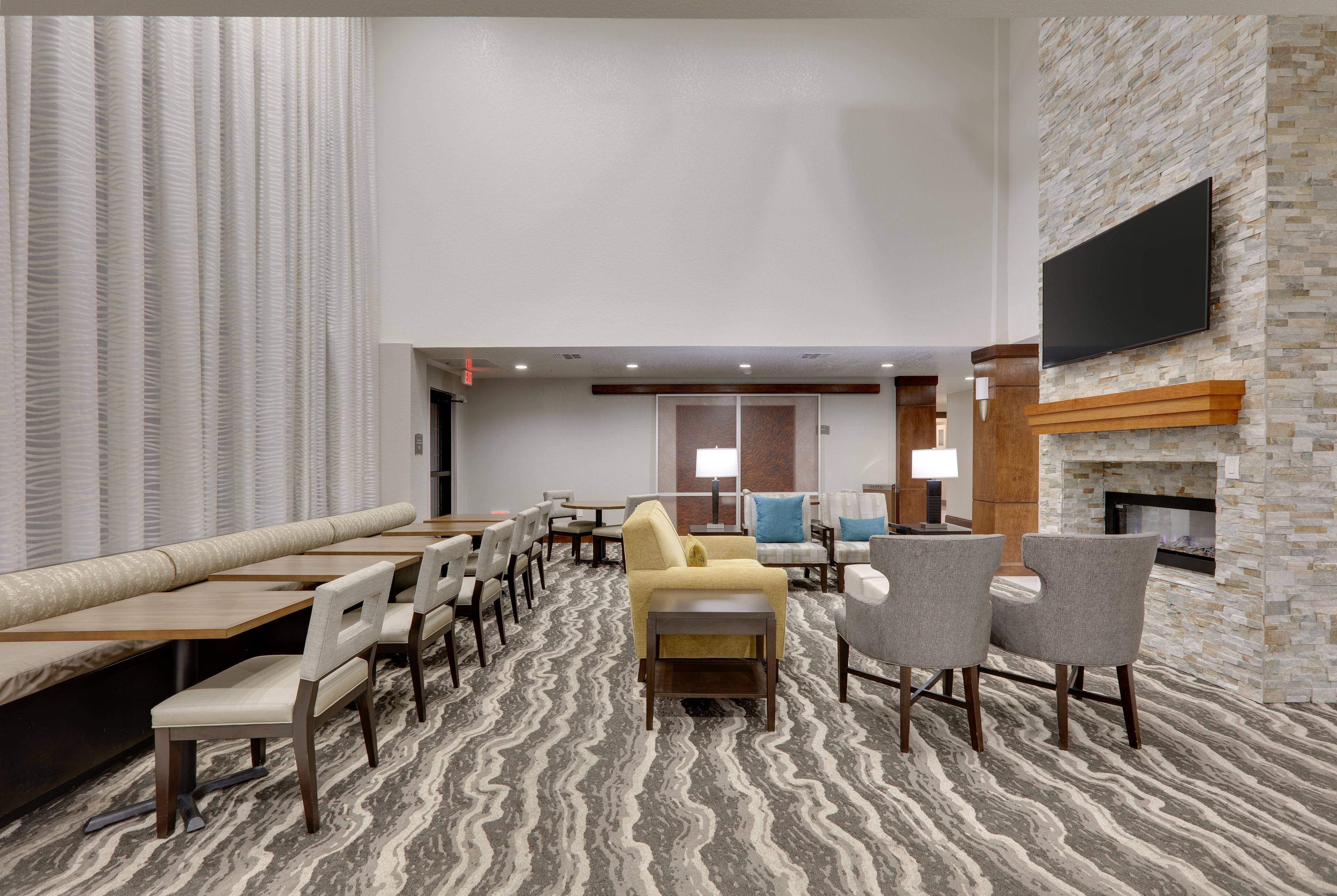 A hotel lobby with seating arrangements, a fireplace, and a television mounted on a stone wall.
