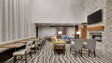 A hotel lobby with seating arrangements, a fireplace, and a television mounted on a stone wall.