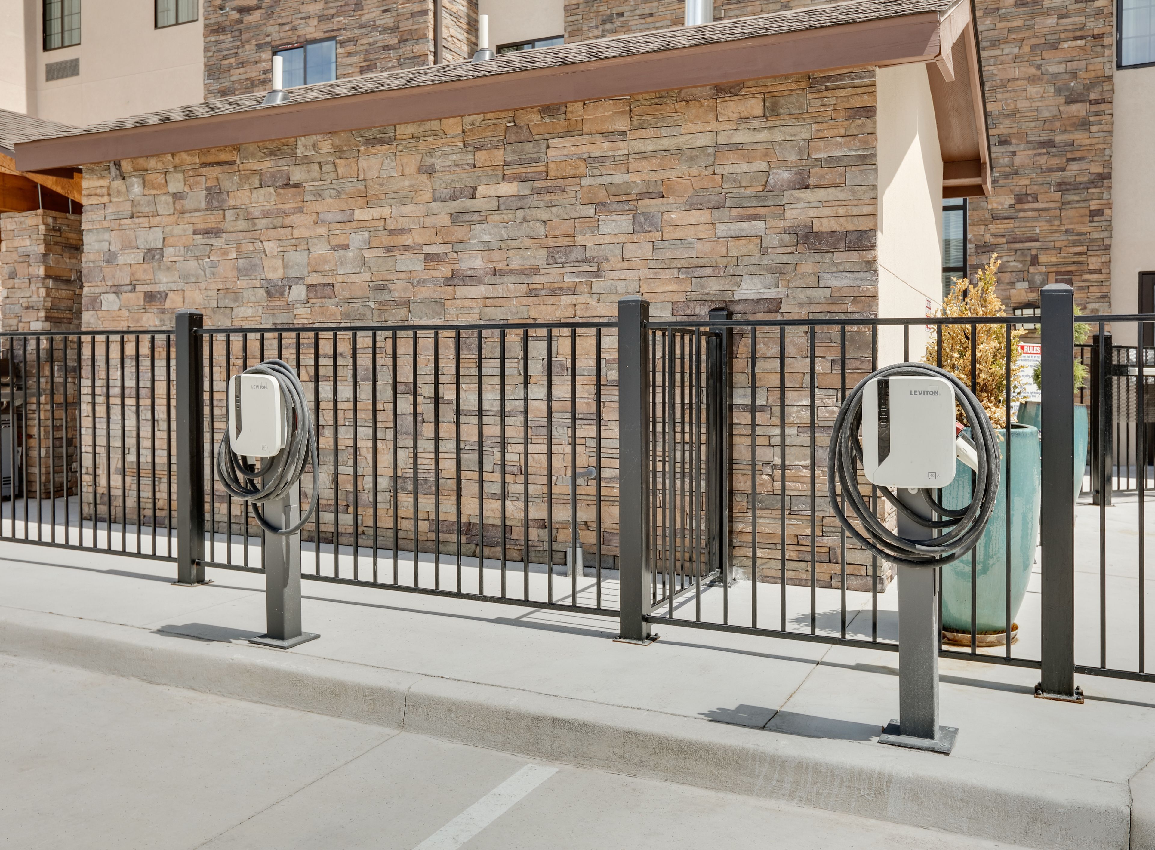 A modern building with a stone facade, a metal fence, and electric vehicle charging stations.