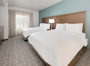 Ein Hotelzimmer mit zwei Betten, einem Nachttisch mit Lampe, einem Schminktisch und einem Fenster mit Vorhängen.