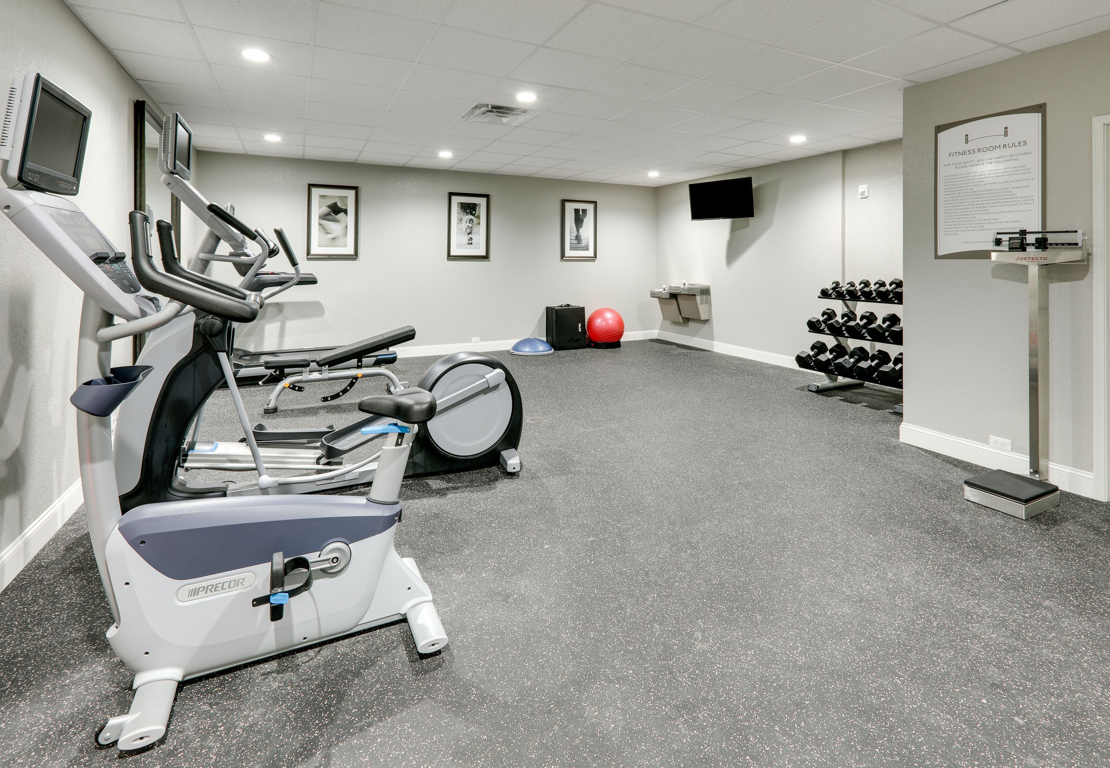 Sala de ginástica com esteiras, bicicleta ergométrica, uma bola de exercício vermelha e um suporte com halteres.