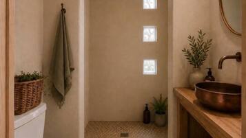 A bathroom with a white toilet, a wooden vanity with a copper basin, a small potted plant, and a towel hanging on the wall.