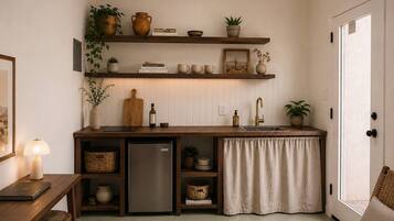 Une cuisine compacte équipée d’un réfrigérateur, d’étagères en bois et d’un coin repas avec une table et des chaises.