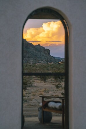 A view through a window with a mountain landscape and a chair outside.