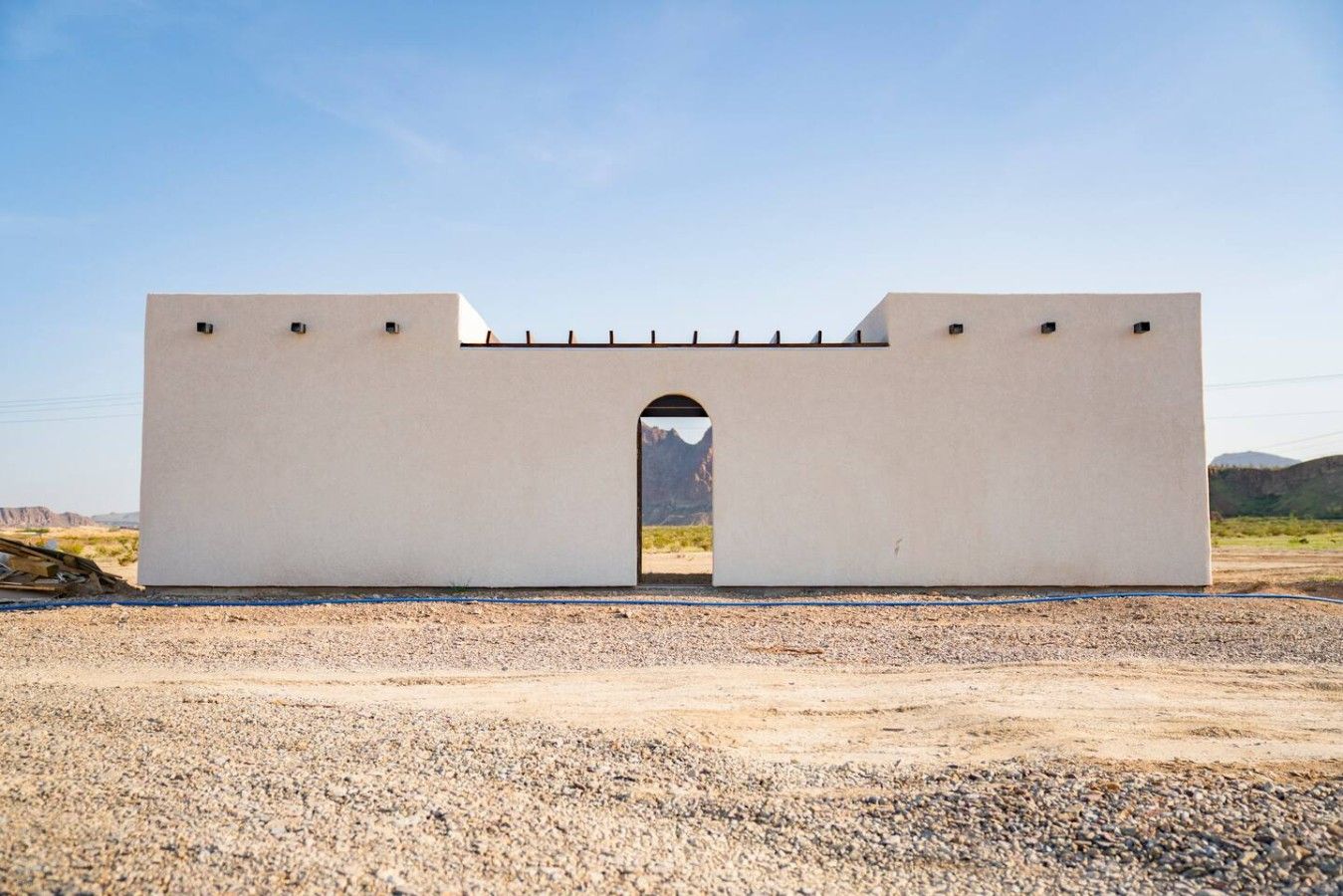 Een groot, wit, rechthoekig gebouw met een centrale boog, gelegen in een kaal landschap met bergen op de achtergrond.