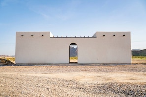 Una gran estructura blanca y rectangular con un arco central, ubicada en un paisaje árido con montañas al fondo.