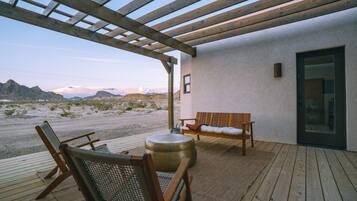 A wooden deck with a bench and chairs, a round table, and a view of a desert landscape.