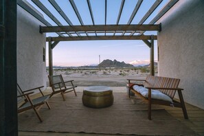 An outdoor patio with a pergola, two wooden chairs, a round table, and a view of a mountainous landscape.