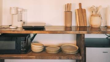 A kitchen with wooden shelves holding mugs, a coffee maker, a cutting board, and a Galanz refrigerator.