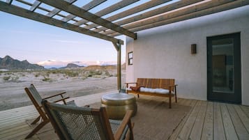 A wooden deck with a bench and chairs, a round table, and a view of a desert landscape.