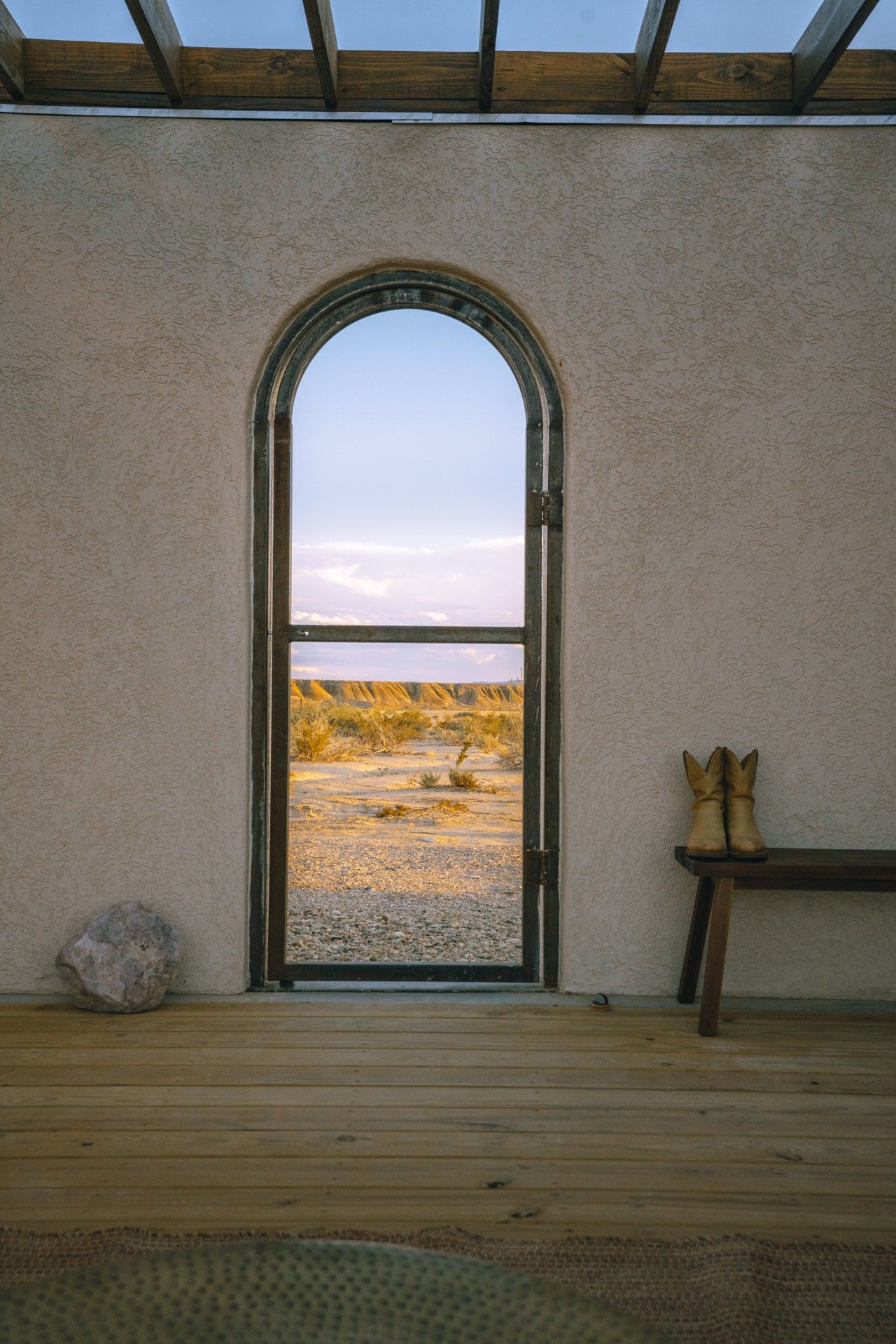 Una habitación con suelo de madera, un banco y un amplio arco que da a un paisaje exterior.
