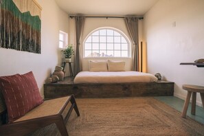 Un dormitorio con una cama, una ventana, una planta y un banco de madera.