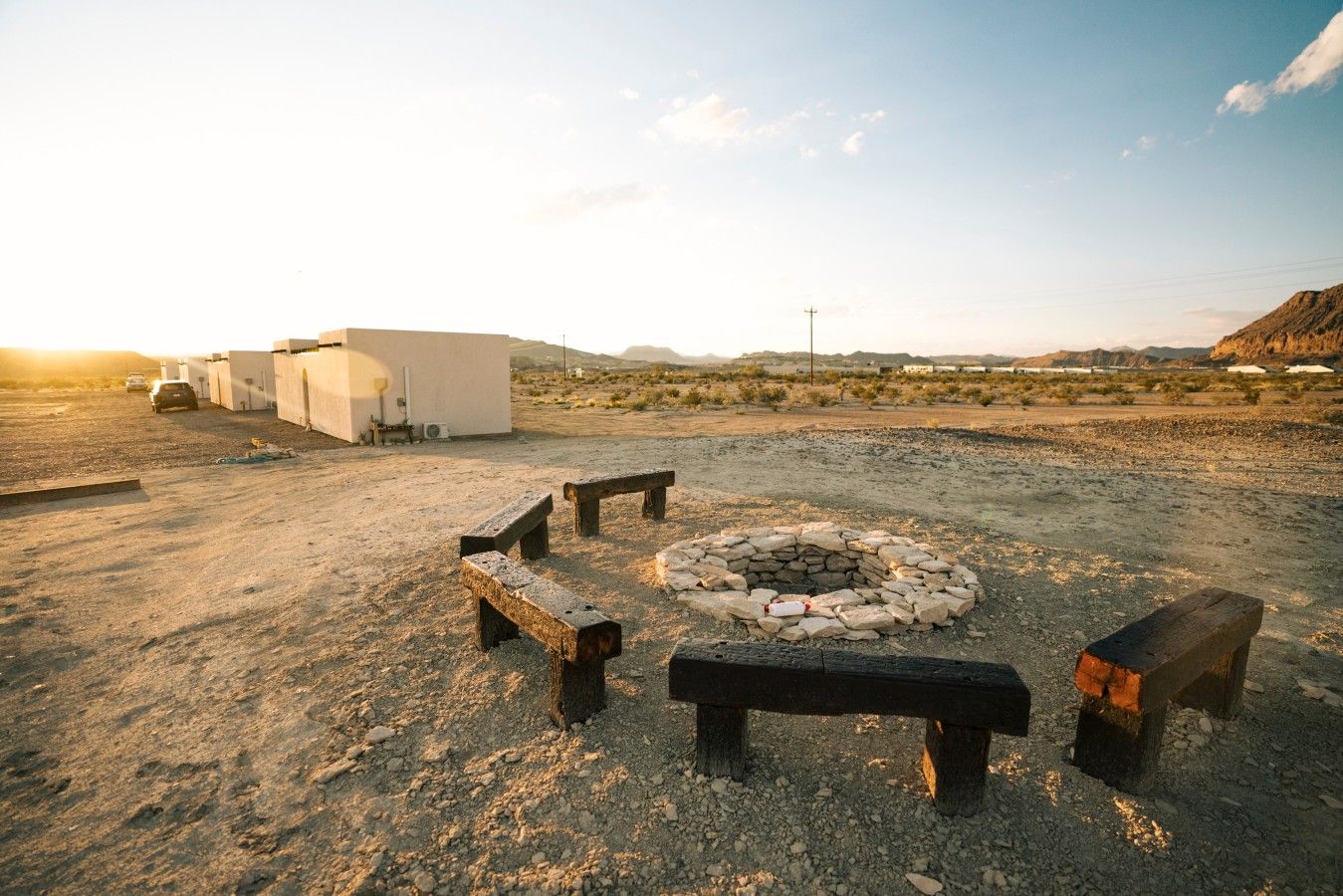 A desert landscape with a fire pit and benches, a white building, and a clear sky.